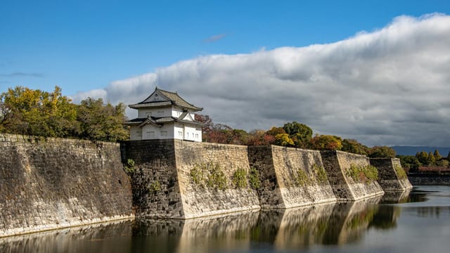 Scenic view of Osaka Castle walls reflecting on the calm moat water under a bright sky.