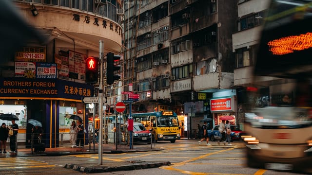 A lively street scene in Hong Kong, showcasing local shops, busy traffic, and pedestrians.