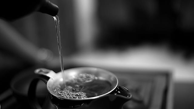 Elegant black and white photo of hot tea being poured into a cup, highlighting the fluid motion and steam.