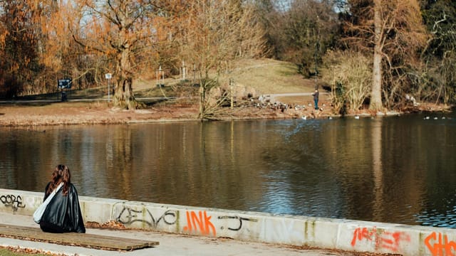 A woman sits by a lake in Düsseldorf park, enjoying a peaceful spring day.