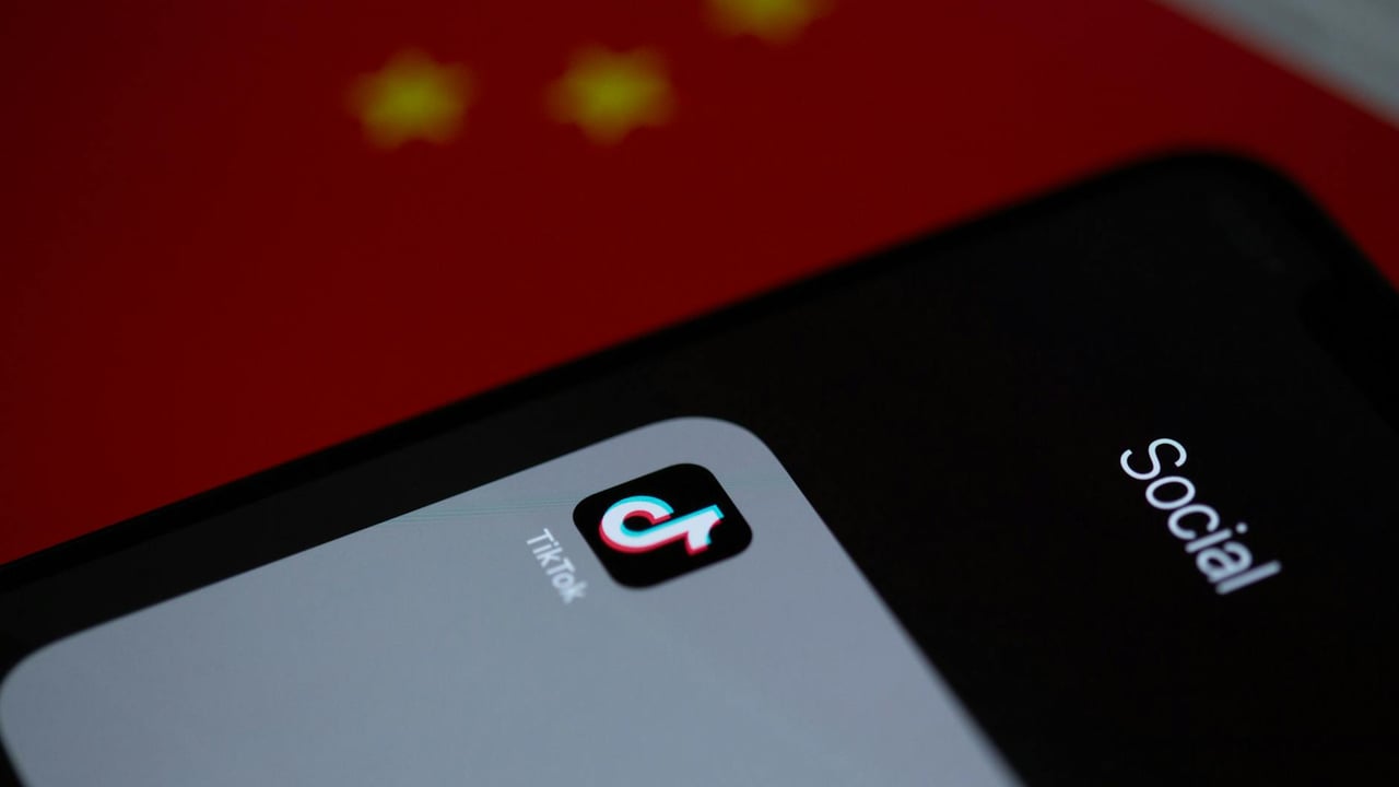 Close-up of TikTok app icon on a smartphone, set against a Chinese flag background.