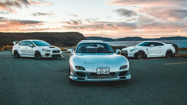 Three luxury sports cars parked outdoors with a stunning sunset backdrop.