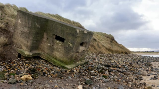 An abandoned WWII bunker on a rocky coastline, showcasing historical architecture.