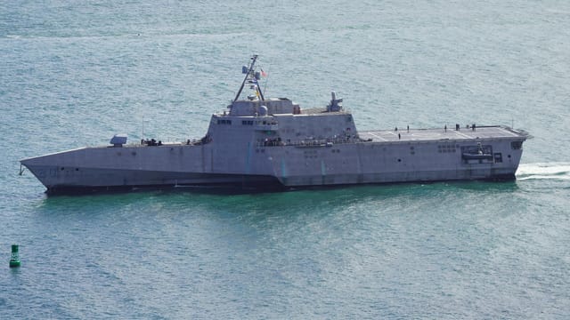 Aerial shot of a modern navy warship cruising through San Diego Bay under clear skies.