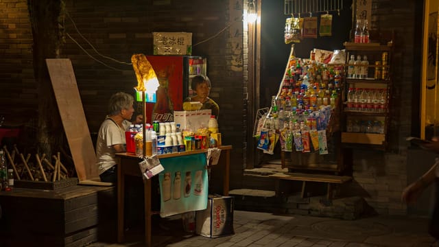 A vibrant night market stall illuminated by lights, offering drinks and snacks.