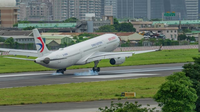 A China Eastern airplane landing on a runway with a city skyline in the background.