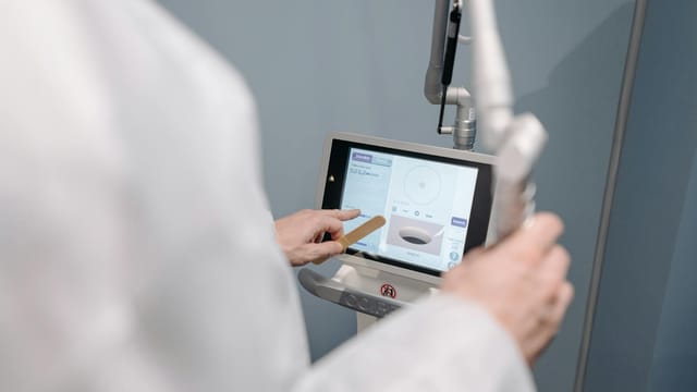 A medical professional using a laser machine with a touch screen interface in a clinical setting.