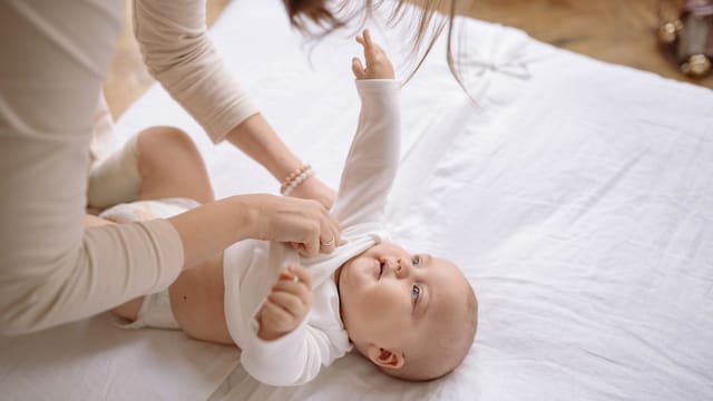 A tender moment of a mother lovingly dressing her baby in a cozy indoor setting.