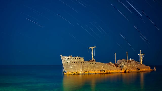 Dramatic capture of a shipwreck illuminated under a serene night sky with visible star trails.