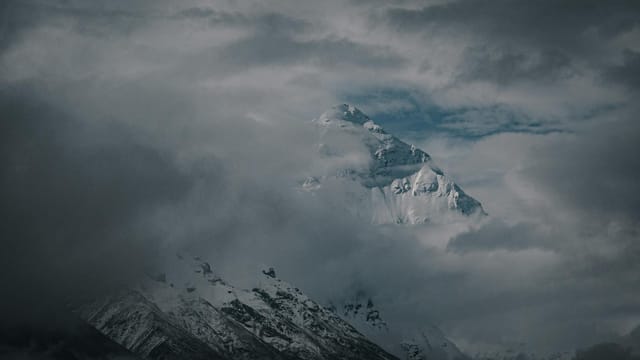 Discover the awe-inspiring view of a snow-capped mountain peak piercing through dense clouds in Tibet, capturing the essence of winter wonder.