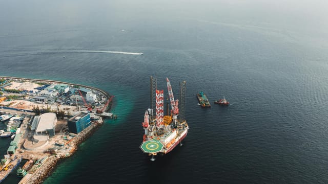 High angle view of an offshore oil rig near a developed coastline. Environmental and industrial themes.
