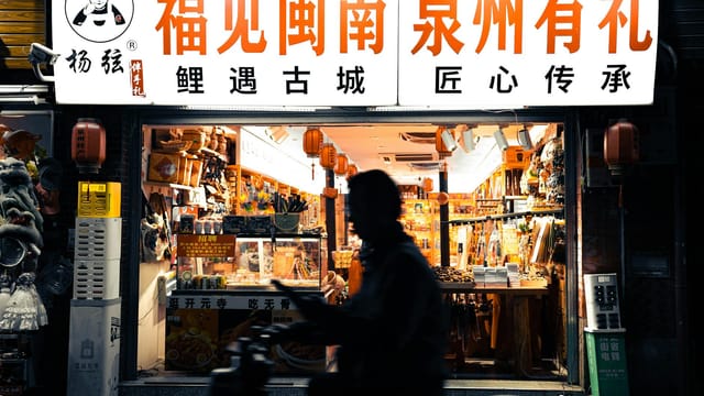 Silhouette of a person passing a vibrant night market shop in Quanzhou, China.