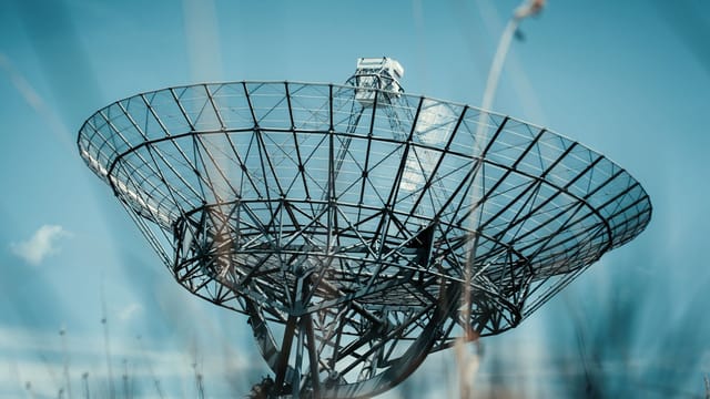 A large satellite dish tower set against a clear blue sky, symbolizing communication technology.