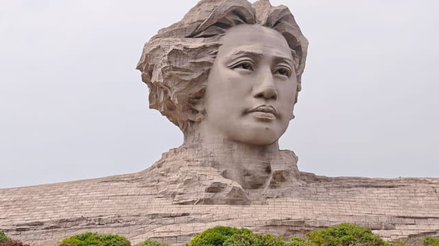 Majestic stone statue of young Mao Zedong on scenic Orange Isle, surrounded by lush greenery.