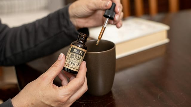 Close-up of hands using hemp extract oil with dropper into a cup indoors.