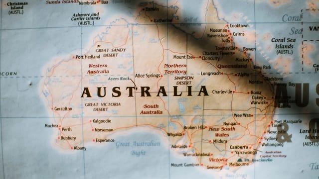 Closeup of political map of Australia with cities and regions with borders surrounded by seas and oceans placed on wall in sunny room