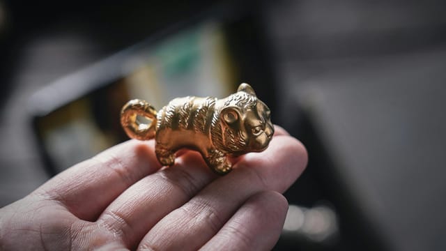 Detailed close-up of a hand holding a small golden tiger figurine with a blurred background.