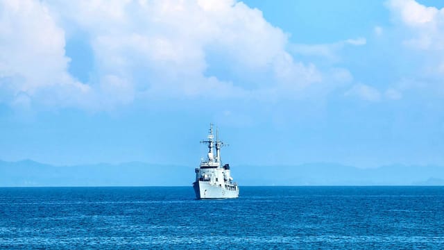 A solitary ship sails through the serene ocean under a bright blue sky with clouds.