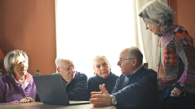 Group of senior adults discussing around a laptop in a warm indoor setting.
