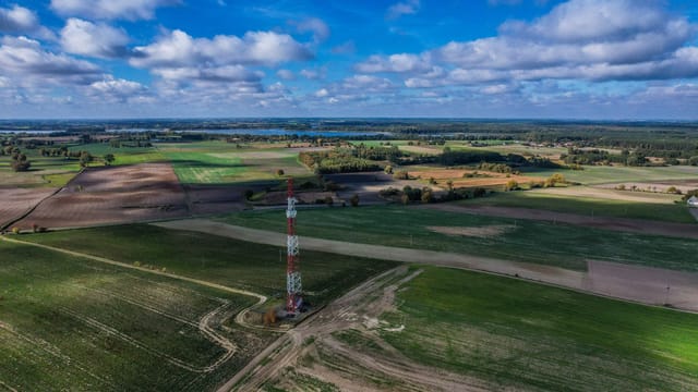 Expansive rural farmland landscape featuring a solitary radio tower under a vibrant blue sky.