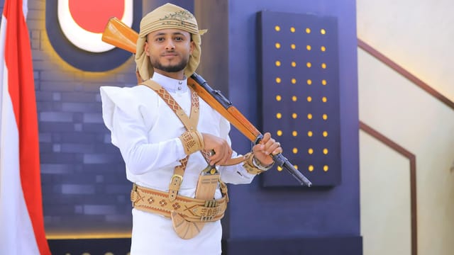 A man in traditional Yemeni dress poses with a rifle indoors in Sana'a, Yemen.