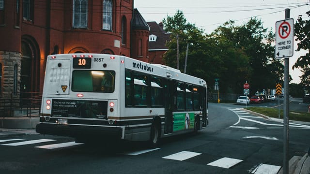 A metrobus rides through urban streets near red brick buildings at dusk, reflecting public transit in a cityscape.