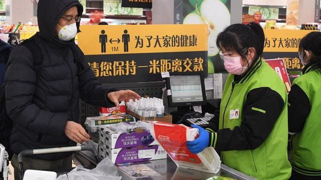 Shoppers wearing masks check out groceries at a Wuhan supermarket, practicing social distancing.