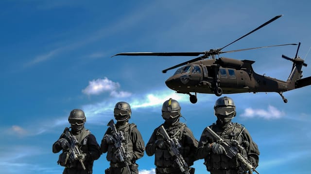 Special forces soldiers in tactical gear with helicopter overhead under a blue sky.