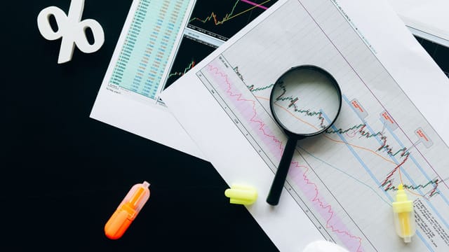 High-angle view of financial charts, showcasing stock market analysis with magnifying glass and highlighters.