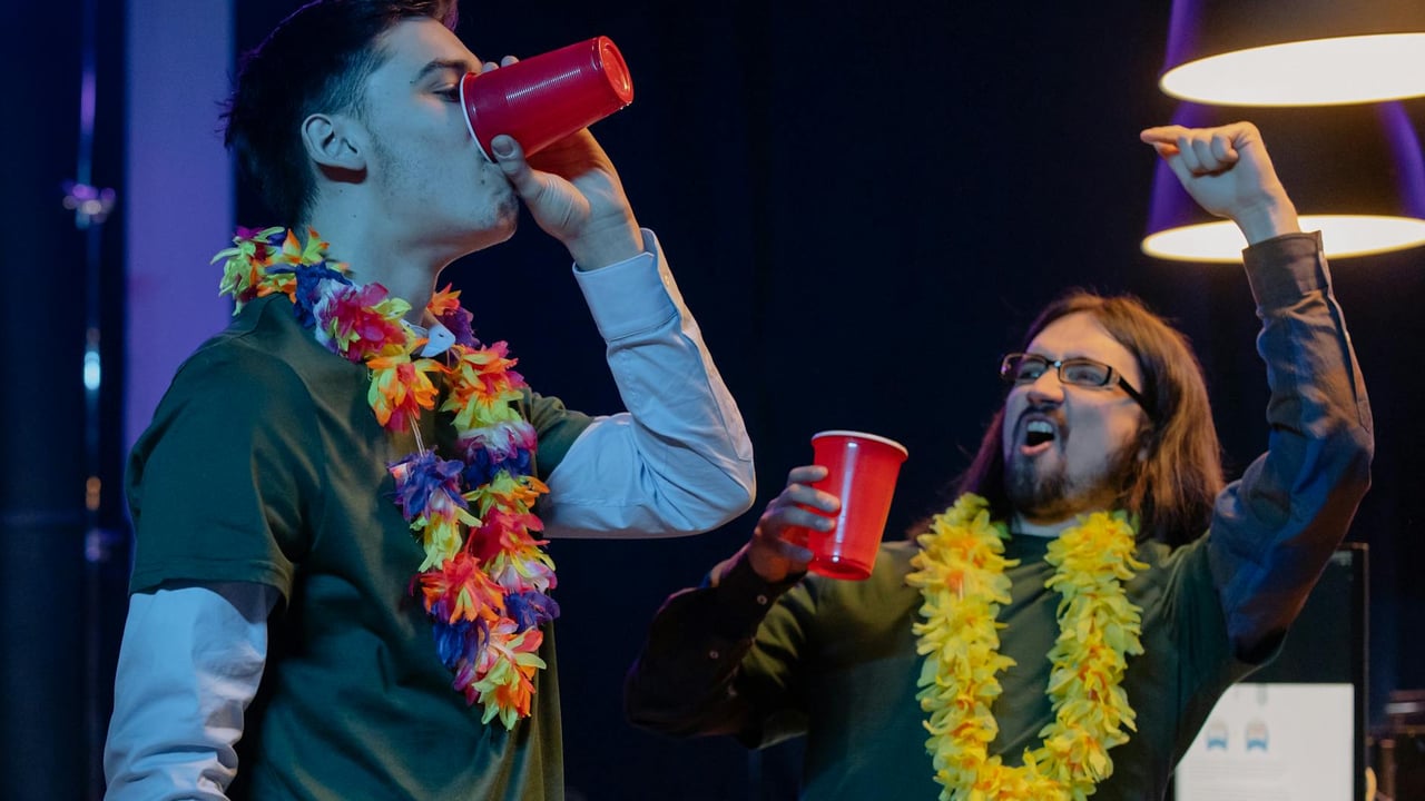 Two men celebrating at an office party with leis and red cups, exuding excitement.