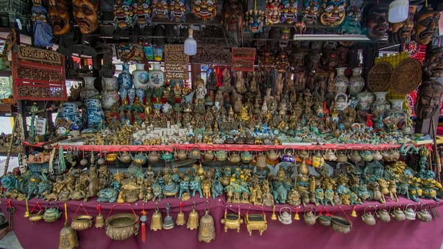 A vibrant outdoor market stall displaying Asian artifacts, masks, and other cultural items.