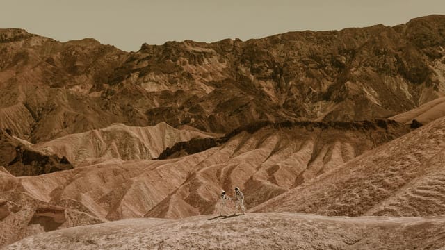 Two astronauts walking on a desolate, rocky landscape resembling Mars.