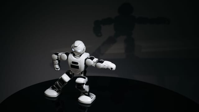 A futuristic white toy robot striking a pose in a dimly lit studio with a shadow cast behind it.