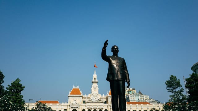 Iconic Ho Chi Minh statue with City Hall in backdrop on a clear day in Vietnam.