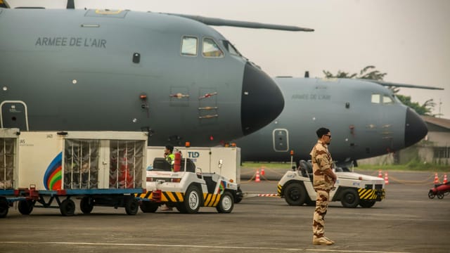 Military personnel near French Air Force planes at an airfield. Cargo loading in progress.