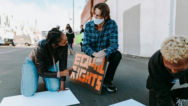 Demonstrators creating protest signs advocating for equal rights on urban street.
