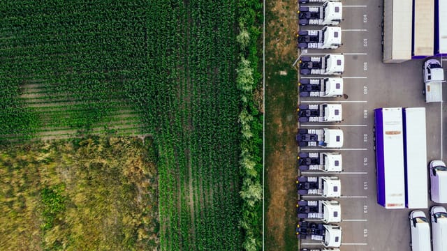Drone shot of parked trucks next to a lush green cropland in Poznań, Poland.