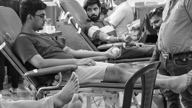 Men donating blood in a healthcare setting, grayscale photography.