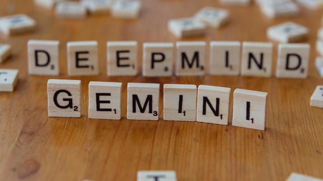 Wooden Scrabble tiles spelling 'Deepmind' and 'Gemini' on a wooden surface, a concept of AI and games.
