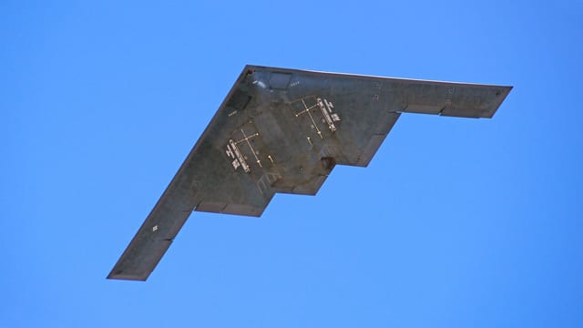 A B-2 stealth bomber from the US Air Force flying against a clear blue sky.