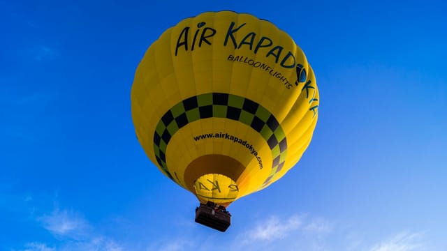 Yellow hot air balloon soaring above Cappadocia's blue sky, Turkey.