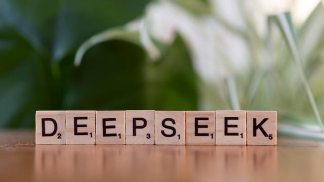 Wooden letter tiles spelling 'DEEPSEEK' on a table with a blurred green background.