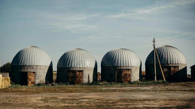 Four dome-shaped abandoned silos stand in a rural Russian field under a clear sky.