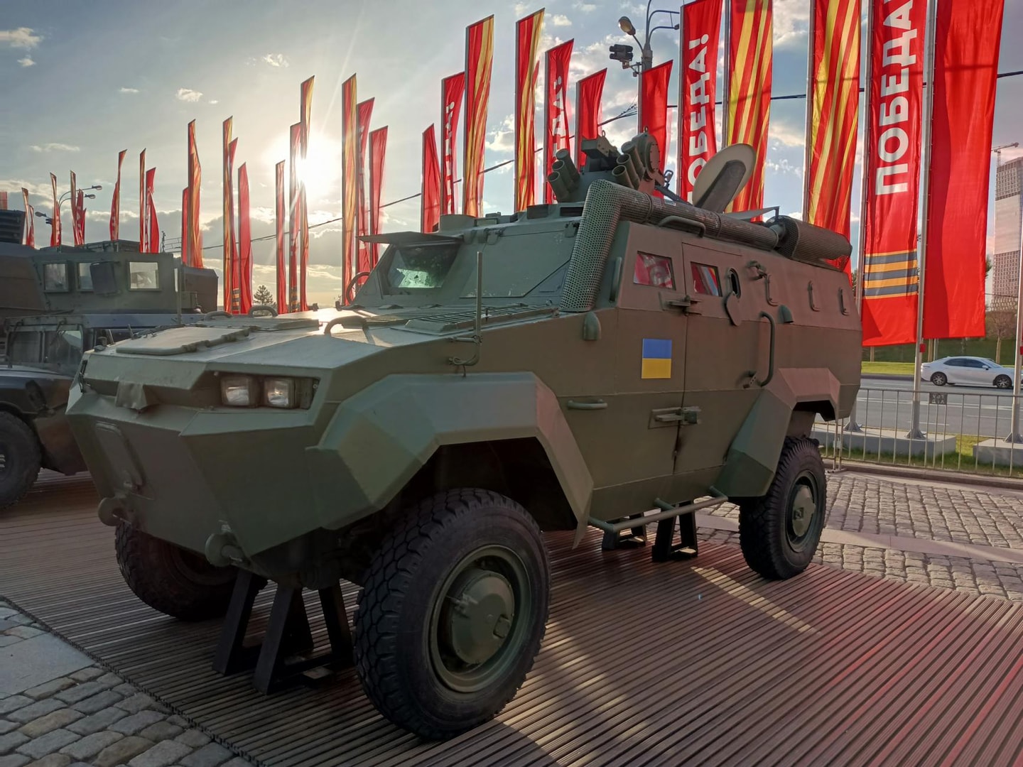 An armored military vehicle showcased outside with flags and sunlight in Moscow.