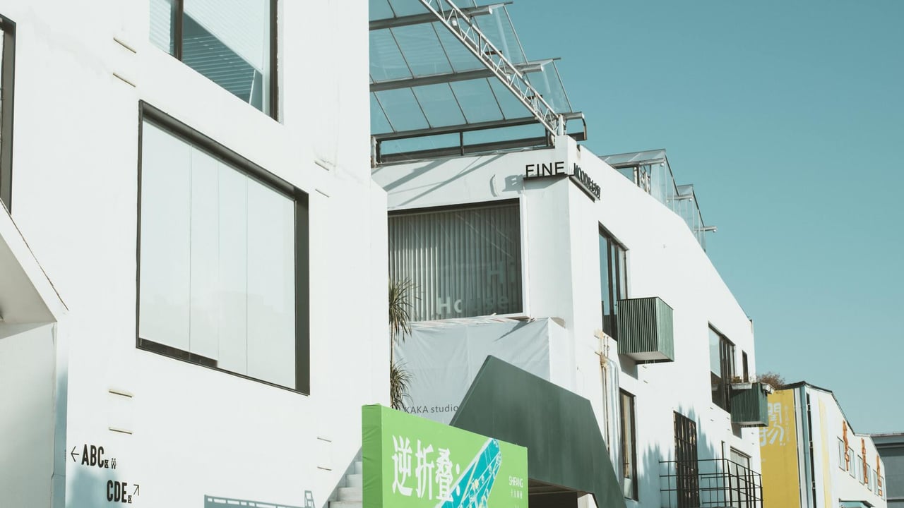 Contemporary white concrete building with glass windows and minimalist design under a clear blue sky.