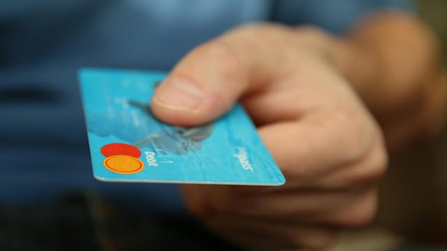 A close-up shot of a hand offering a blue debit card for payment.