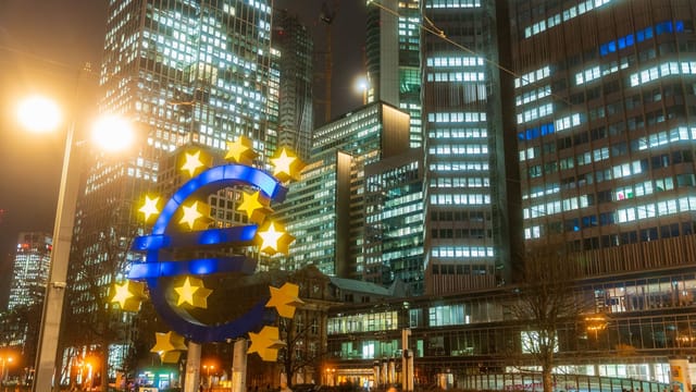 Night view of the iconic Euro sculpture in Frankfurt's bustling financial district.
