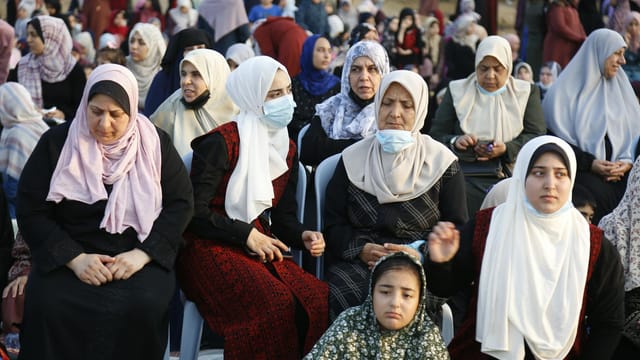 A group of women in hijabs pray together outdoors in the Gaza Strip, captured during daylight.