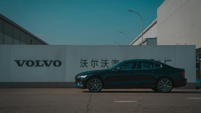 Sleek black Volvo sedan parked outside a manufacturing plant with Volvo signage.