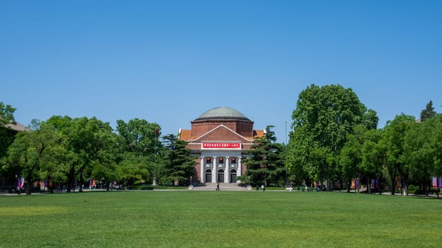 A classic brick university building surrounded by a green lawn and trees under a clear blue sky.